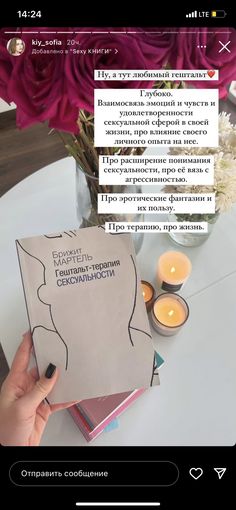someone is holding up a book on the table with candles in front of them and flowers behind it