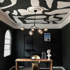 a dining room with black walls and an artistic ceiling design painted on the wall above it