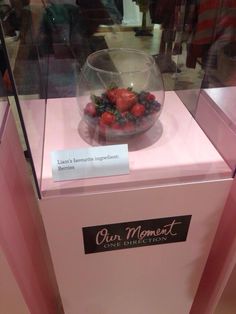 a glass bowl filled with strawberries on top of a pink display case in a store