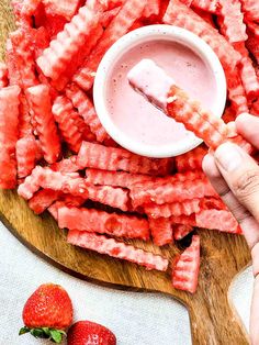 someone is dipping something into a bowl with strawberries on the table next to it