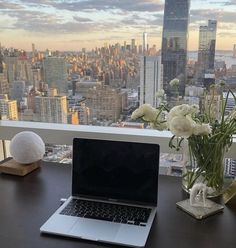 an open laptop computer sitting on top of a desk next to a vase with flowers