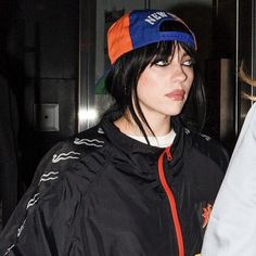 a woman with black hair wearing a blue hat and jacket while standing next to another woman