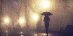 a person with an umbrella standing in the rain under street lights at night on a rainy day