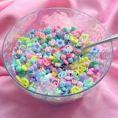 a glass bowl filled with lots of colorful beads and plastic letters on top of a pink cloth