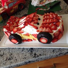 a cake decorated with strawberries and chocolate on a white plate next to a toy car