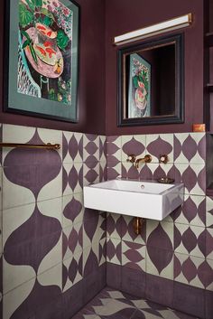 a bathroom with purple and white tiles on the walls, two framed pictures above the sink