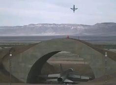 an airplane is flying in the sky over a road and bridge with mountains in the background