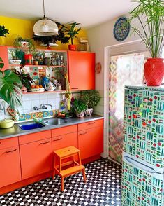 a kitchen with orange cabinets and black and white checkered flooring, potted plants on the wall