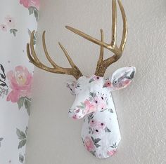 a deer head mounted to the wall with flowers on it's back and gold antlers