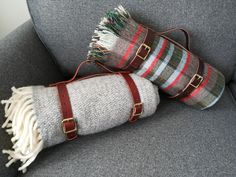 two blankets are sitting on the back of a couch with leather straps and buckles