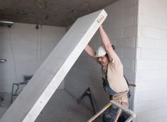 a man in overalls and a hard hat is holding up a large piece of concrete