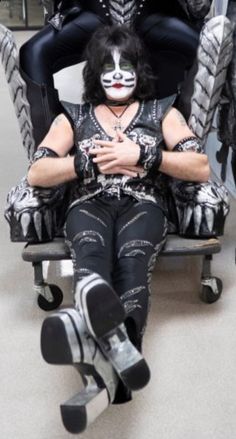 a man sitting on top of a chair next to two women in black and white makeup