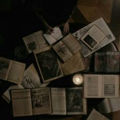 an overhead view of many open books on the floor with one candle lit in front of them