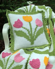 a crocheted blanket and two pillows are sitting on a white chair with flowers