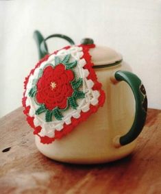 a crocheted tea pot cover sitting on top of a wooden table next to a mug