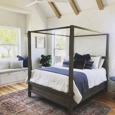 a bedroom with white brick walls and wood flooring has a four poster bed in the center