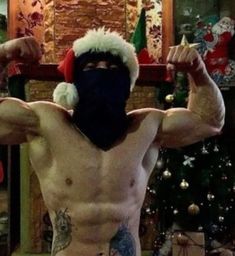 a shirtless man wearing a santa claus hat and holding up his arms with both hands