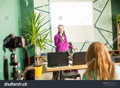 a woman giving a presentation in front of a group of people with laptops on the table