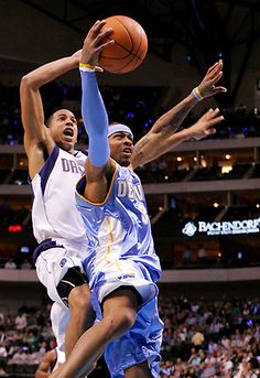 two men are playing basketball in front of an audience at a sporting event, one is jumping for the ball