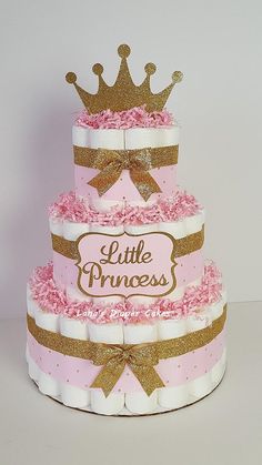 a three tiered cake with pink frosting and gold trimmings, topped with a crown