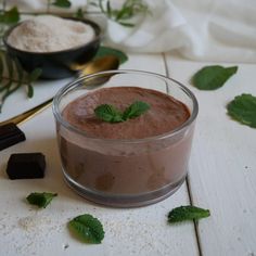 a glass bowl filled with chocolate pudding on top of a white table next to green leaves