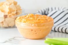 a bowl filled with dip next to some celery and chips on a table