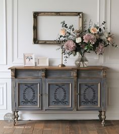 a vase with flowers sitting on top of a wooden dresser next to a mirror and framed photo