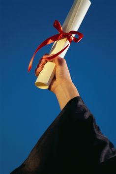 a person holding up a diploma in the air with a red ribbon on it's end