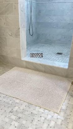 a bathroom with white tile and beige flooring on the shower wall, along with a bathtub in the background