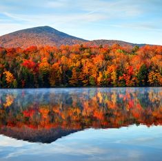 a lake surrounded by trees with fall foliage on the mountains in the backgroud