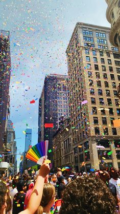 a crowd of people standing in front of tall buildings with confetti falling from the sky