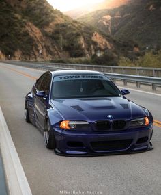 a blue bmw is parked on the side of the road in front of some mountains