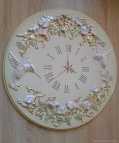 a white clock with birds and flowers on it's face that is hanging from the wall