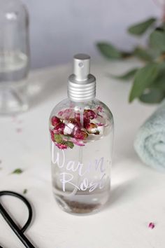 a close up of a bottle of perfume on a table with scissors and flowers in the background