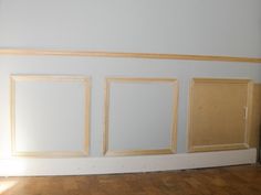 three empty frames on the wall in an empty room with hard wood flooring and bare walls