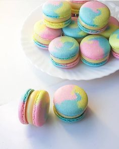 there are many macaroons on the plate and one is pink, blue, yellow and green