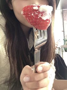 a woman holding a fork with a strawberry on it