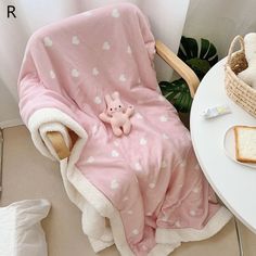 a pink blanket sitting on top of a white table next to a basket with bread