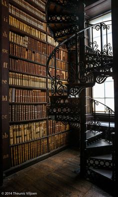 a spiral staircase in front of a bookshelf filled with lots of old books