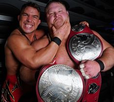 two men hugging each other with their arms around one another and holding the same wrestling belts