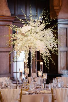 a tall vase filled with white flowers sitting on top of a table covered in glasses