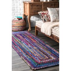 a multicolored area rug in front of a bed with pillows and blankets on it