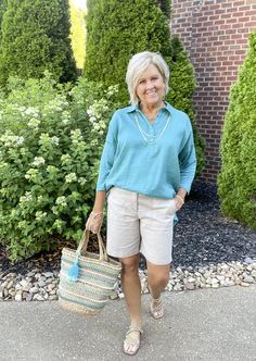 a woman standing in front of some bushes holding a basket and smiling at the camera