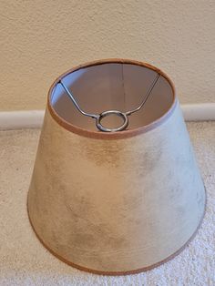 a lamp shade sitting on the floor in front of a wall with a ring hanging from it