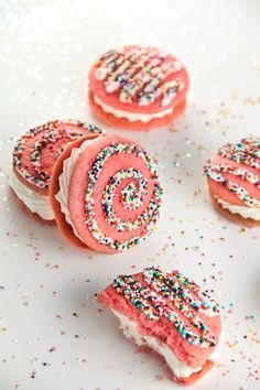 some pink and white cookies with sprinkles on them sitting on a table