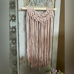 a pink macrame hanging on a door with flowers in the vase next to it