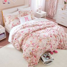 a bedroom decorated in pink and white with flowers on the comforter, bedding and pillows