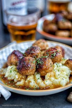 some meatballs and mashed potatoes on a white plate with a glass of beer in the background
