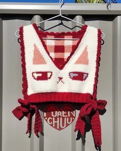 a red and white knitted sweater hanging from a clothes rack with sunglasses on it