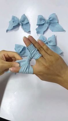 two hands holding small blue bows on top of a white surface with one hand in the air